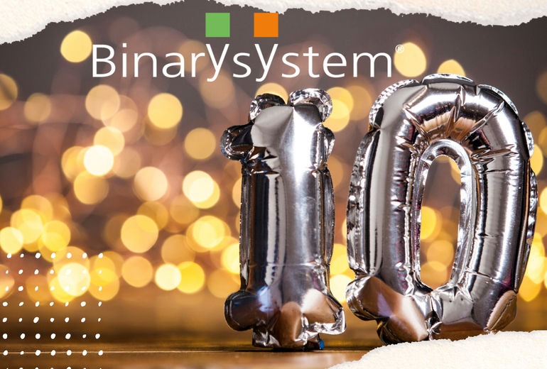 Celebratory image with the logo of BinarySystem at the top, featuring silver foil balloons in the shape of the number 10, symbolizing a 10-year anniversary. The background is decorated with warm, out-of-focus festive lights, creating a cheerful and celebratory atmosphere.